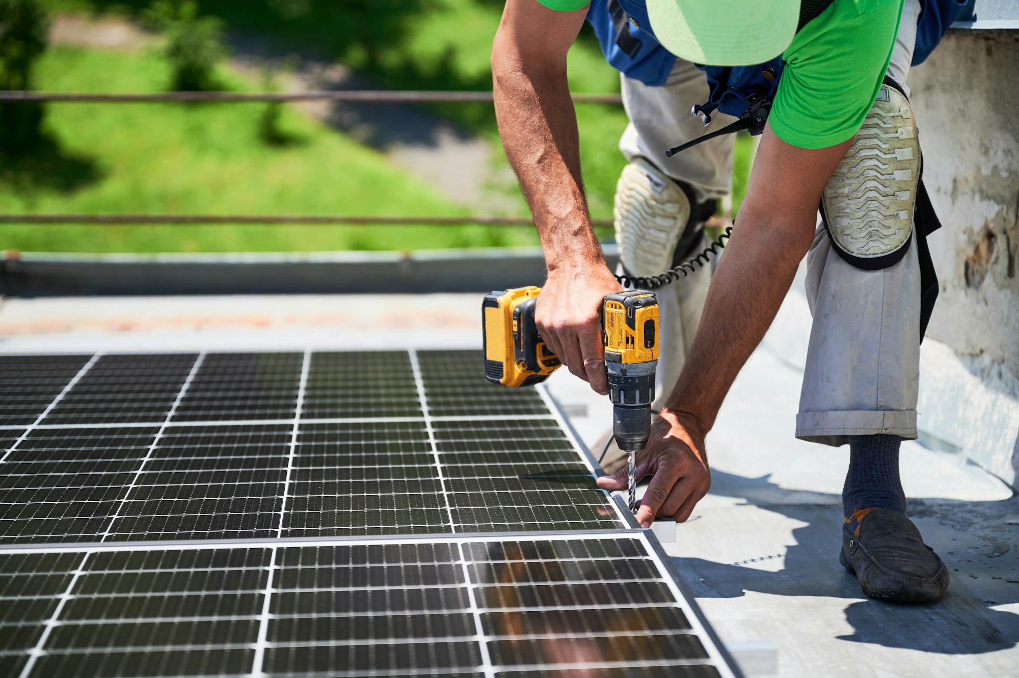 Worker building photovoltaic solar panel system on rooftop of house with help of electric drill.