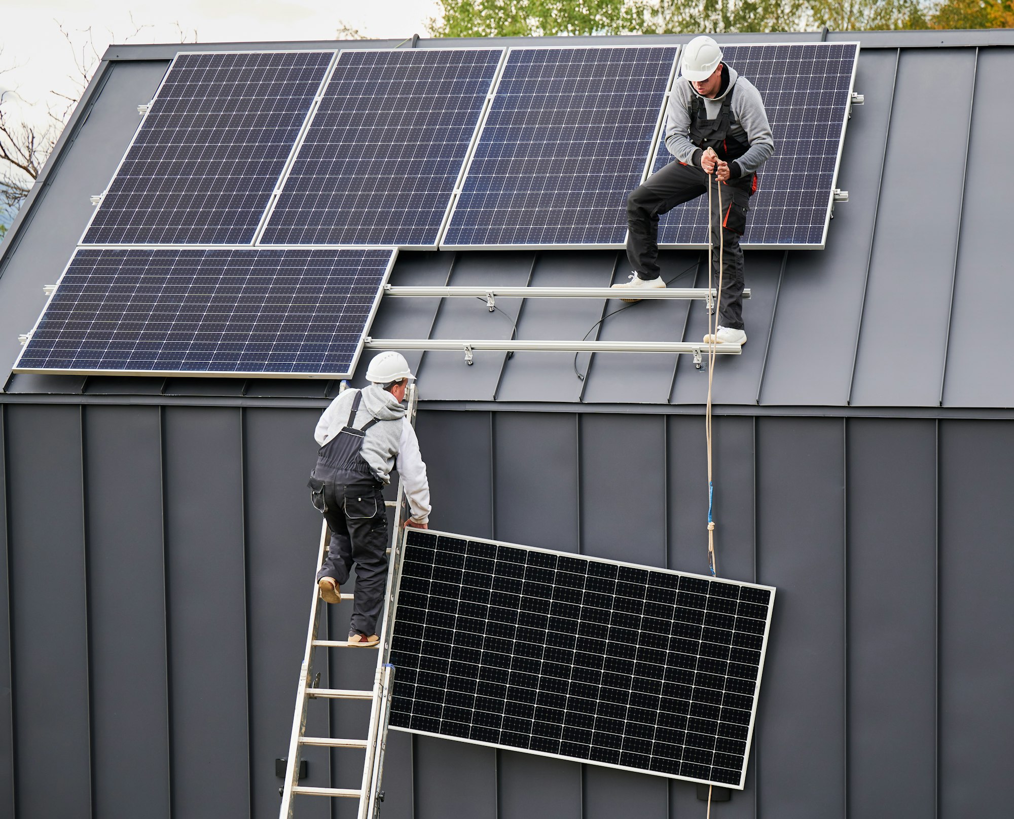 Workers lifting up photovoltaic solar module while installing solar panel system on roof of house.